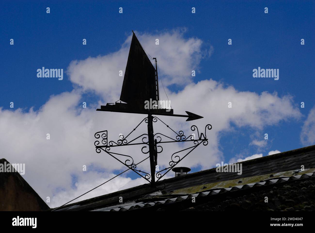 Wetterfahne in Form eines Segelbootes mit Hochsegel in Silhouette vor blauem Himmel und geschwollenen weißen Wolken Stockfoto