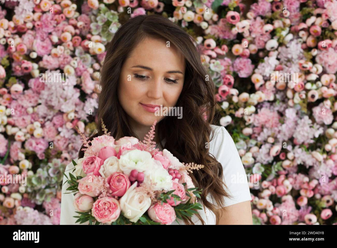 Stilvolles weibliches Modell mit Rosenblume in der Hand, das auf blühendem Blumenblütenhintergrund steht. Liebe, 8. märz, Geburtstag und Feiertagsfrau Porträt Stockfoto