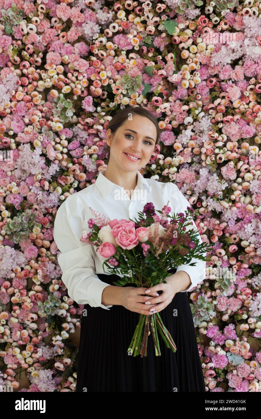 Fröhliche gesunde Frau lächelt und hält bunte rosa Farbe Blumenstrauß auf floralem Frühling oder Sommer Hintergrund, Studio Mode Schönheit Porträt Stockfoto