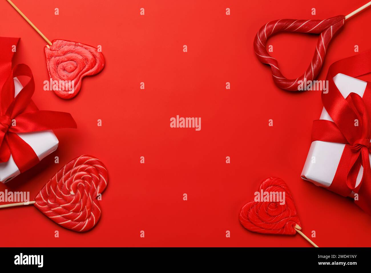 Herz-Lutscher: Süße Leckereien und Geschenkboxen vor rotem Hintergrund mit Textabstand. Flache Valentinskarte Stockfoto