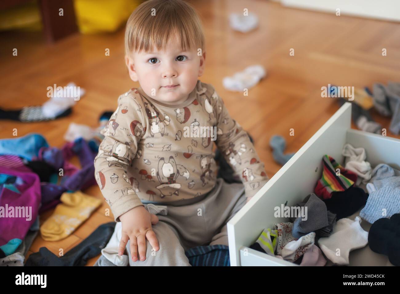 Der glückliche süße und lachende Junge ist völlig vertieft darin, während des Spielens in einem gemütlichen Schlafzimmer Socken zu untersuchen Stockfoto