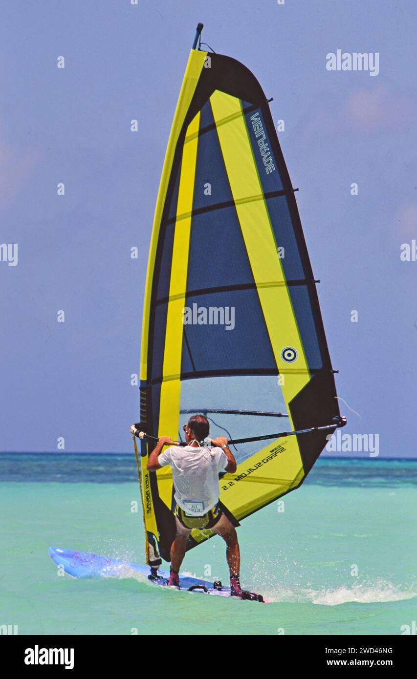 Mann im Urlaub, der perfekte Wetterbedingungen genießt Winsurfen (Boardsegeln) im kristallklaren blauen Wasser vor der Küste von Aruba CA. Anfang der 1990er Jahre Bitte schreiben Sie dem Fotografen Joan Iaconetti zu Stockfoto