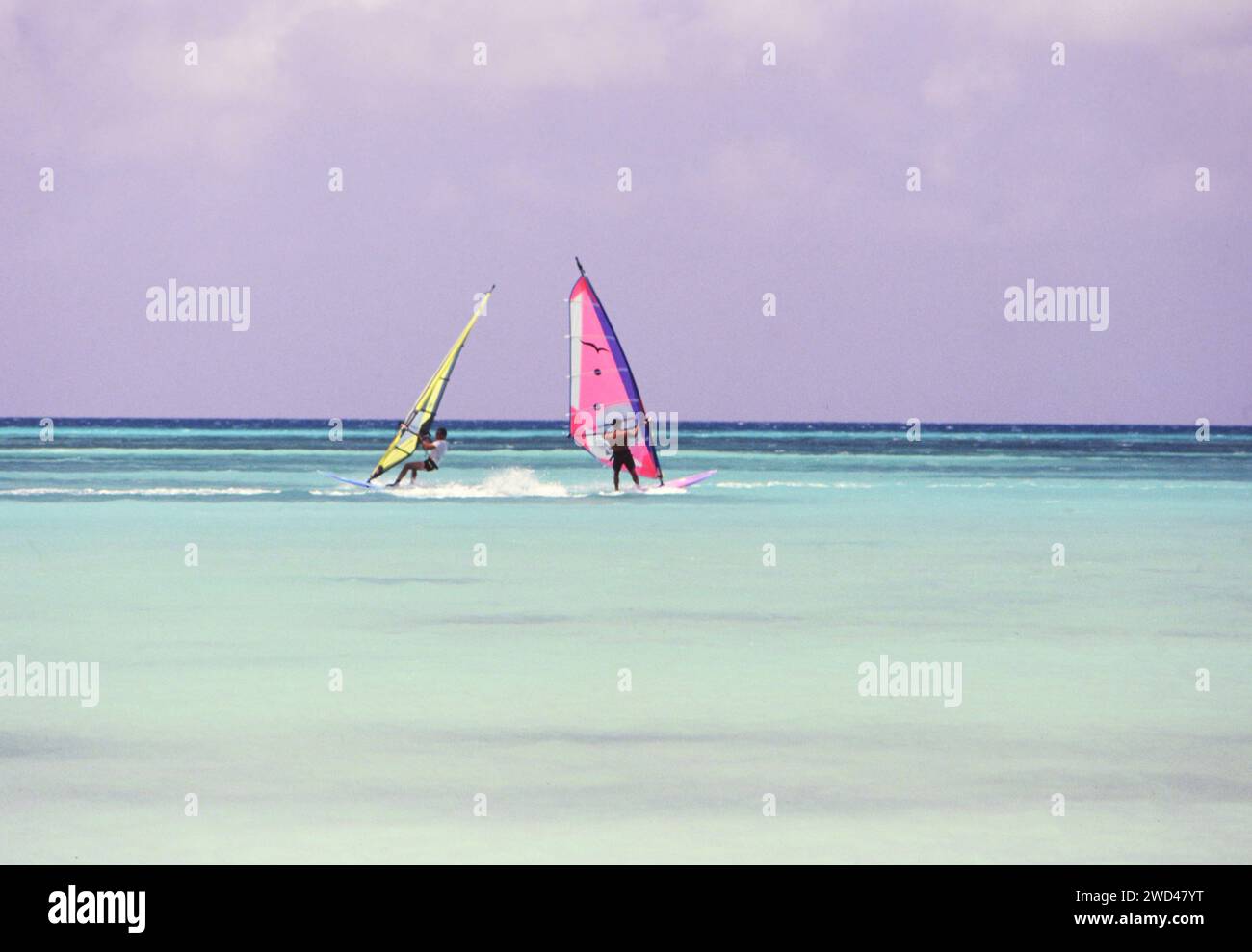 Lange Aufnahme von zwei Windsurfern (Boardsailern), die in den blauen Gewässern vor Aruba CA überquerten. Anfang der 1990er Jahre Bitte schreiben Sie dem Fotografen Joan Iaconetti zu Stockfoto