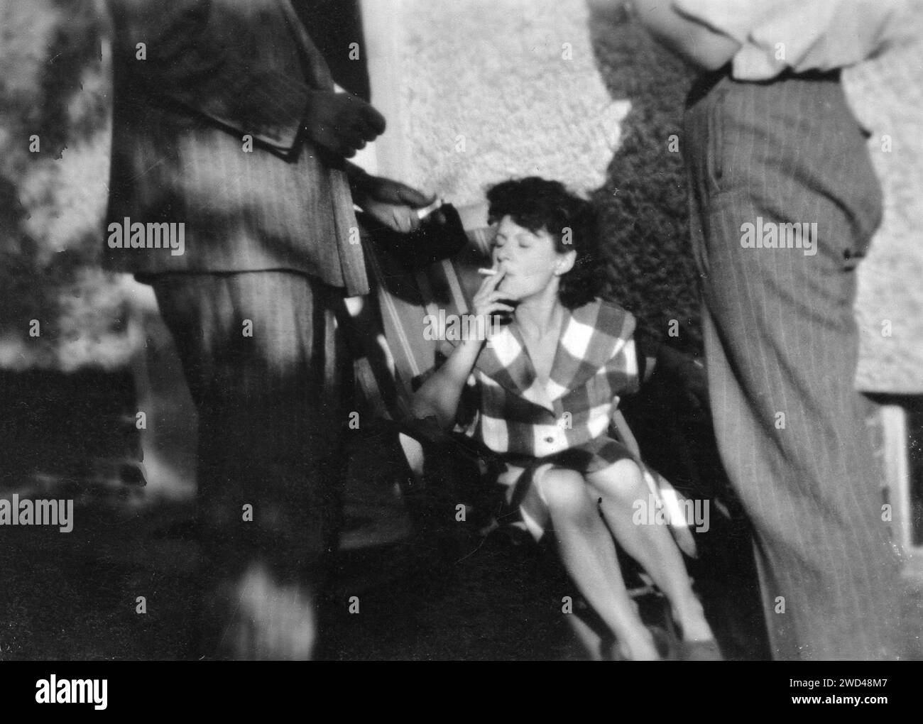 Ein antikes Foto zeigt eine rauchende Frau, die auf einer Chaiselongue sitzt und zwei Männer neben ihr stehen, dargestellt von der Hüfte nach oben. Deutschland. Datum unbekannt Stockfoto