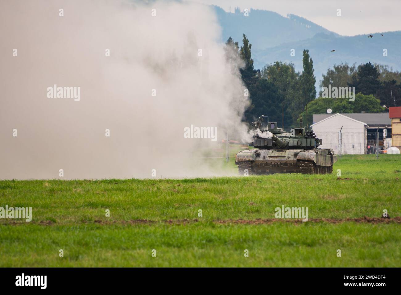 T-72 Kampfpanzer (M4 – CZ-Variante), der seine Hauptkanone auf einem grünen Feld während einer Kriegsspielprobe abfeuert. Stockfoto