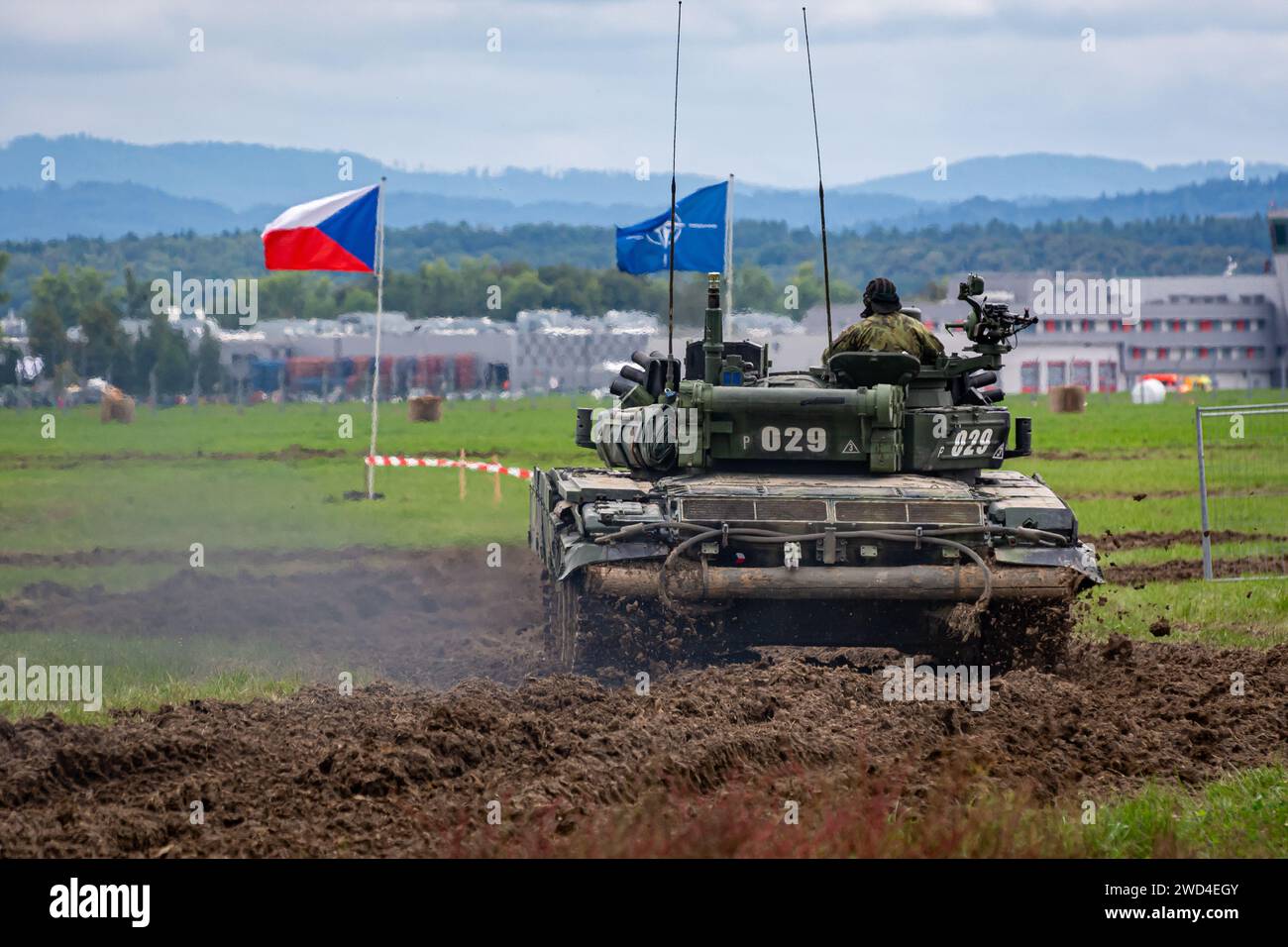 T72 Tank (M4 CZ Variantennummer 029) fährt während einer Demonstrationsübung auf einem schlammigen Feld vor NATO- und Tschechischen Flaggen. Stockfoto