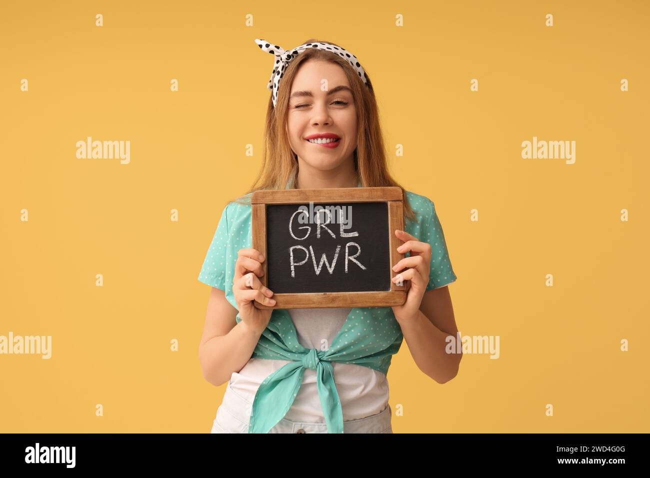 Schöne junge Pin-up-Frau, die Tafel mit Text MÄDCHEN MACHT und beißende Lippe auf gelbem Hintergrund hält Stockfoto
