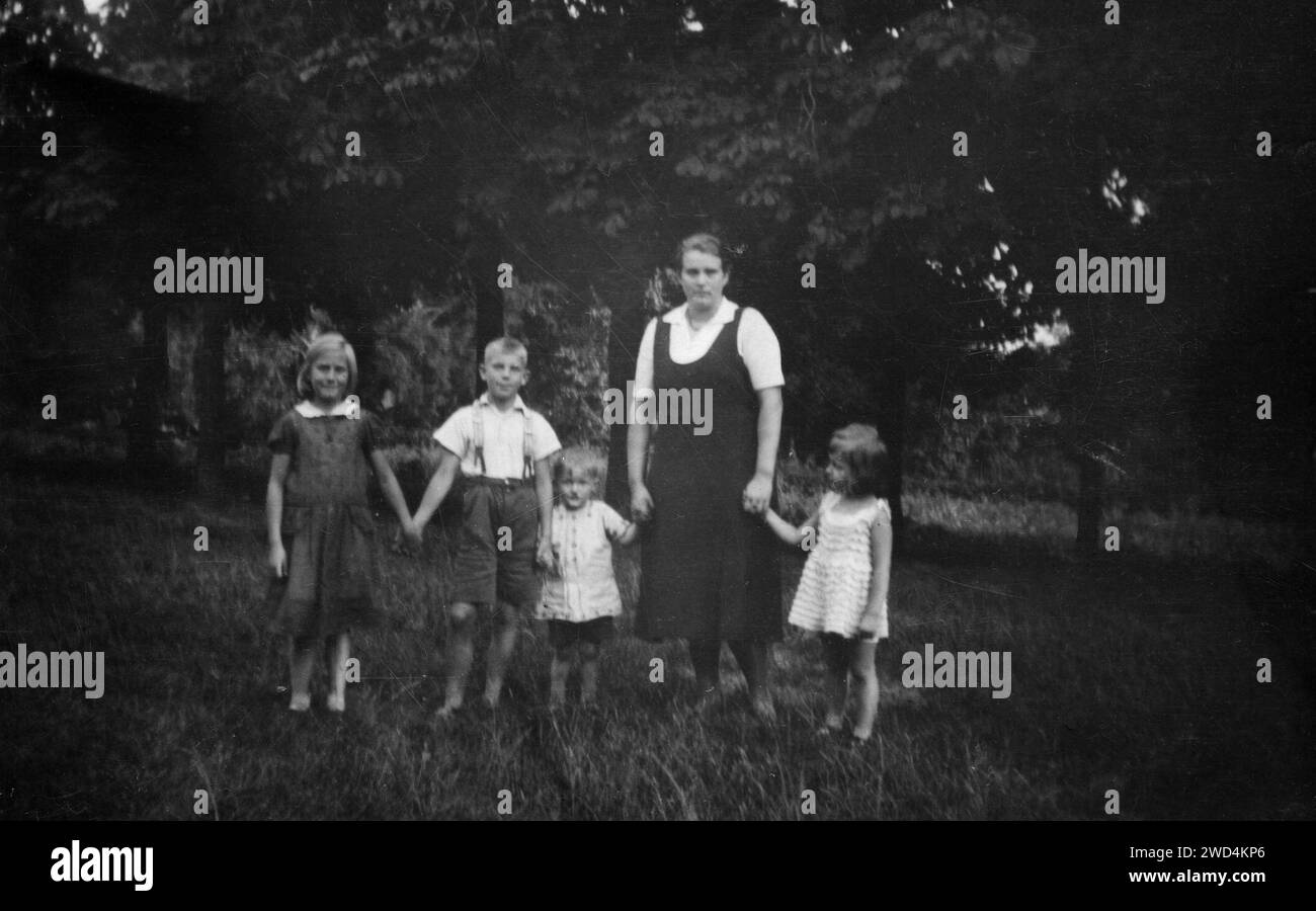 Ein antikes Foto zeigt eine Frau mit zwei Mädchen und zwei Jungen, die im Park vor der Kulisse von Kastanienbäumen posiert. Datum unbekannt, um die 1950er Jahre Stockfoto