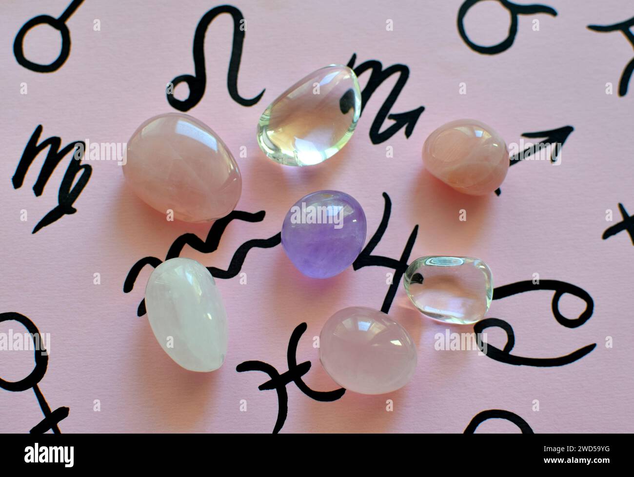 Wunderschöne Amethyst- und Rosenquarzkristalle auf rosa Hintergrund mit Symbolen der Tierkreiszeichen. Stockfoto