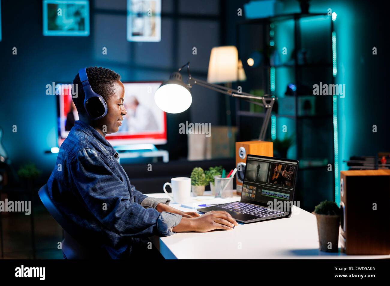 Schwarze Frau mit schnurlosem Headset zum Anhören und Bearbeiten von Audio- und Videoaufnahmen auf ihrem PC. Freelancer mit Kopfhörern und Laptop, der moderne Technologie bei der Erstellung von Inhalten nutzt. Stockfoto