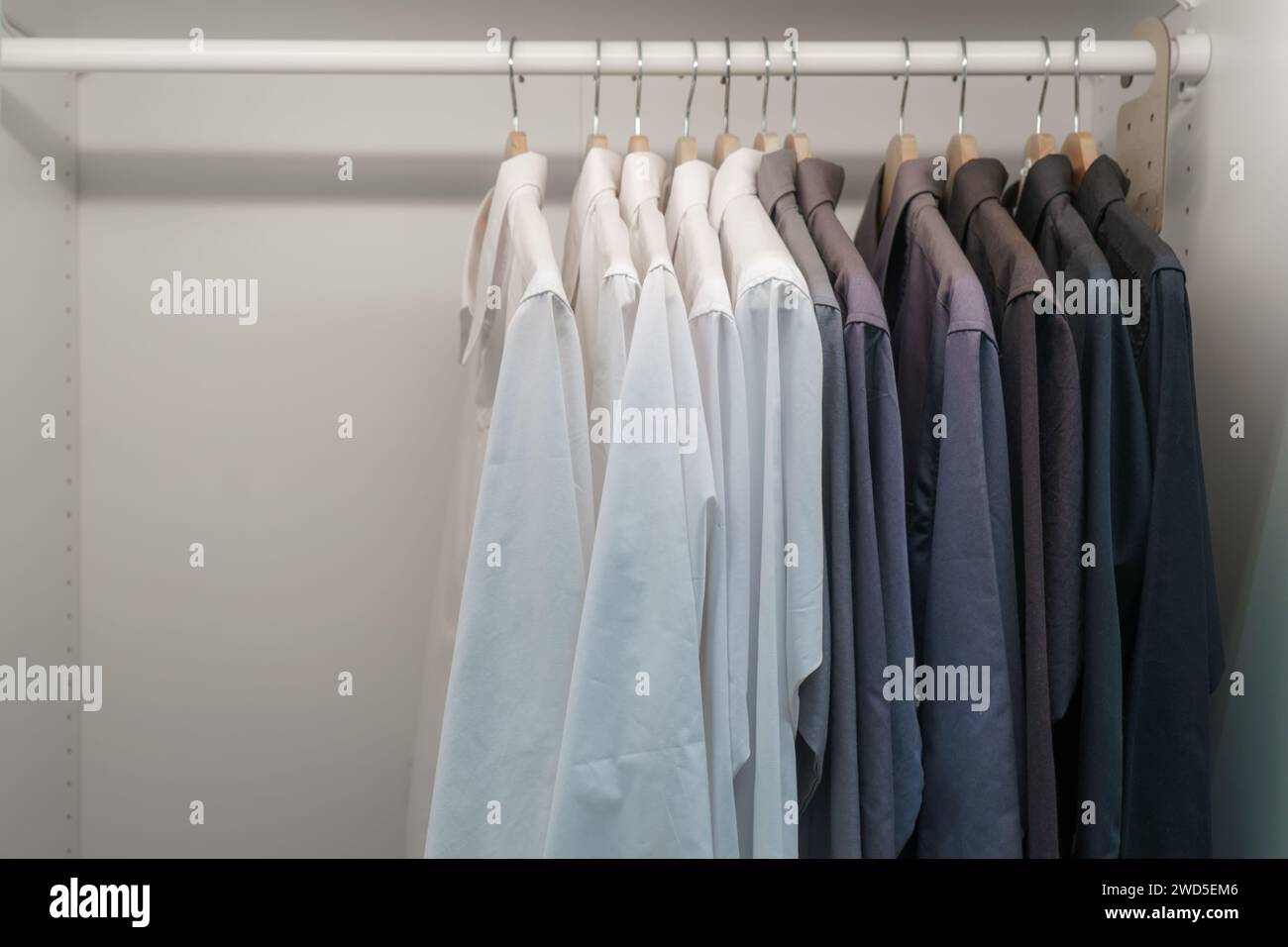 Entdecken Sie den Inbegriff von Raffinesse mit einer Kollektion sorgfältig gehängter Herrenanzüge und -Hemden in einem gut organisierten Schrank. Diese Szene strahlt eine Re aus Stockfoto
