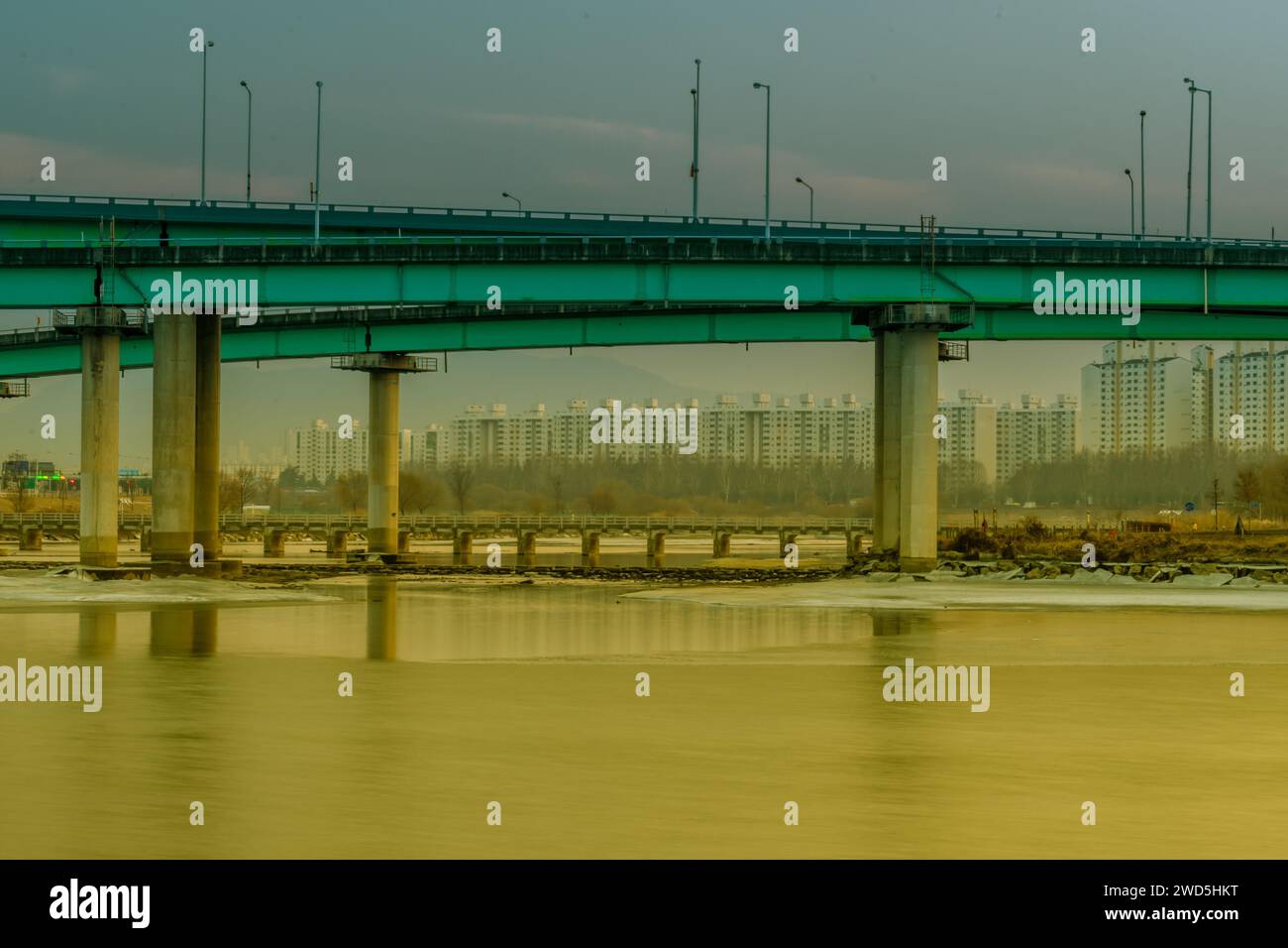 Brücken über teilweise gefrorenen Fluss mit Stadtgebäuden und Bäumen im Hintergrund, Südkorea Stockfoto