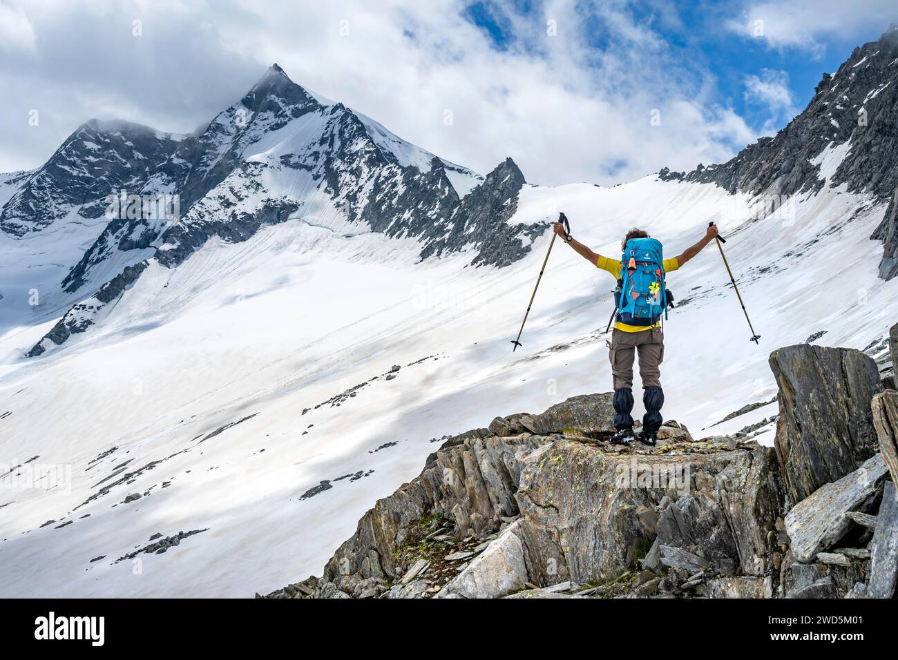 Bergsteigerin auf einem Felsen zwischen Schnee, hebt triumphierend ihre Arme, hinab vom Gipfel des Schönbichler Horns, Blick auf schneebedeckte und verschneite Stockfoto