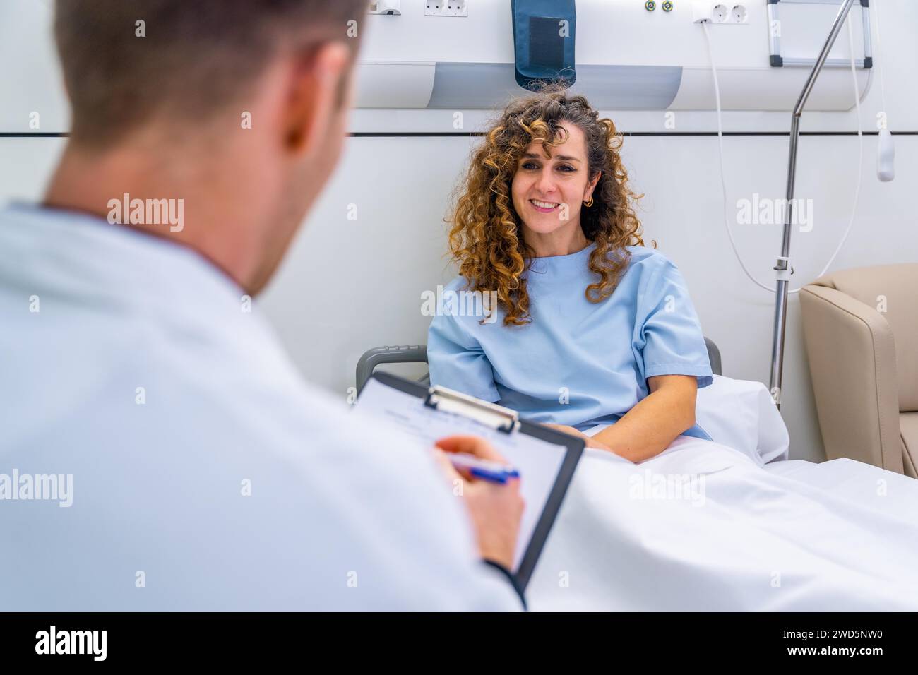 Rückansicht einer nicht erkennbaren Ärztin, die eine Patientin im Krankenhausbett betreut Stockfoto