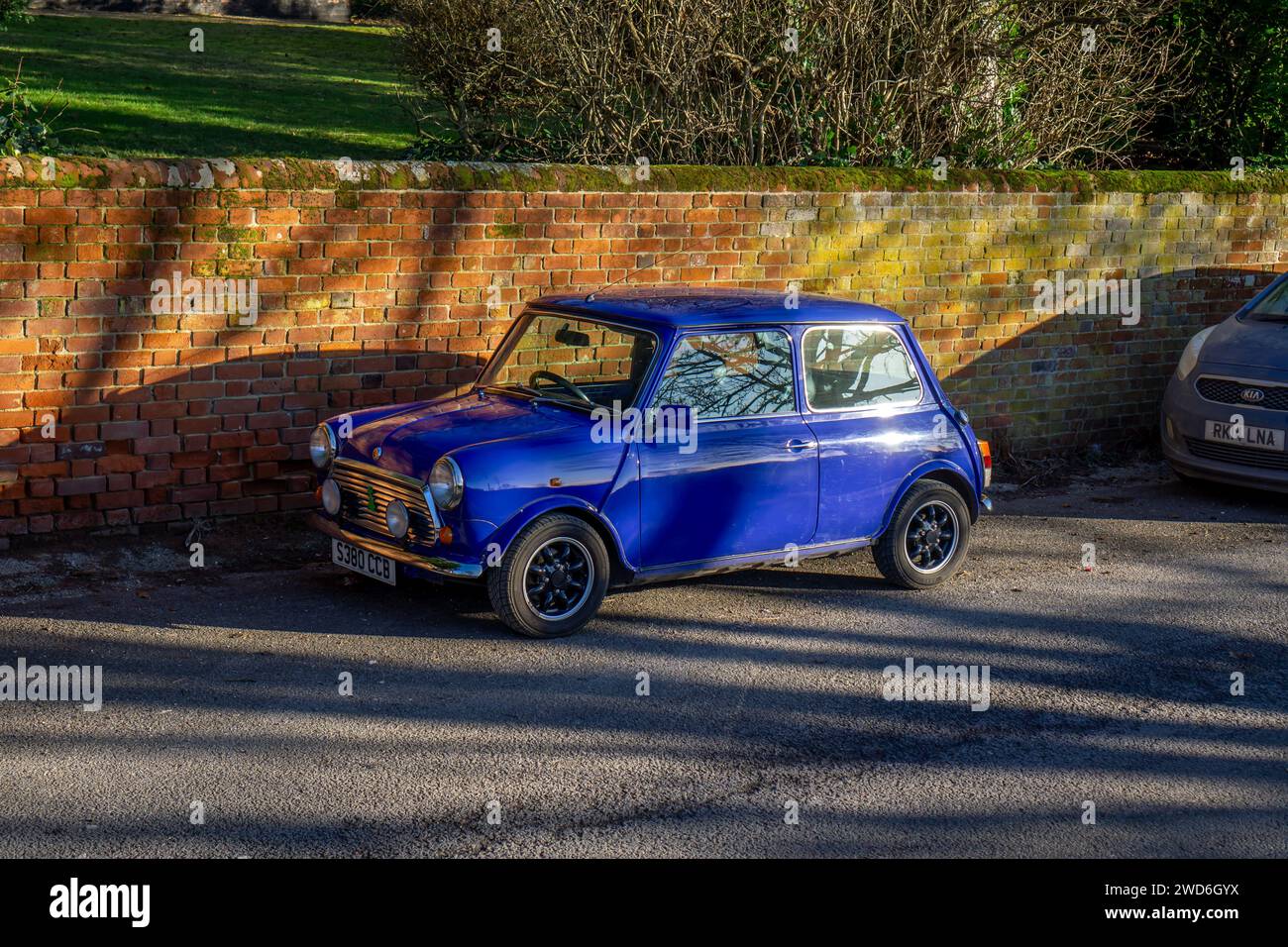 Ein leuchtend blauer klassischer Mini Cooper, der neben einer alten Backsteinmauer in Saffron Walden, Essex, im Sonnenlicht geparkt ist Stockfoto