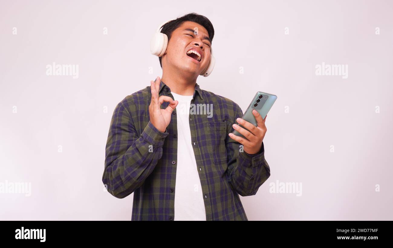 Asiatischer junger Mann, der Musik auf dem Smartphone mit schnurlosen Kopfhörern vor weißem Hintergrund hört Stockfoto
