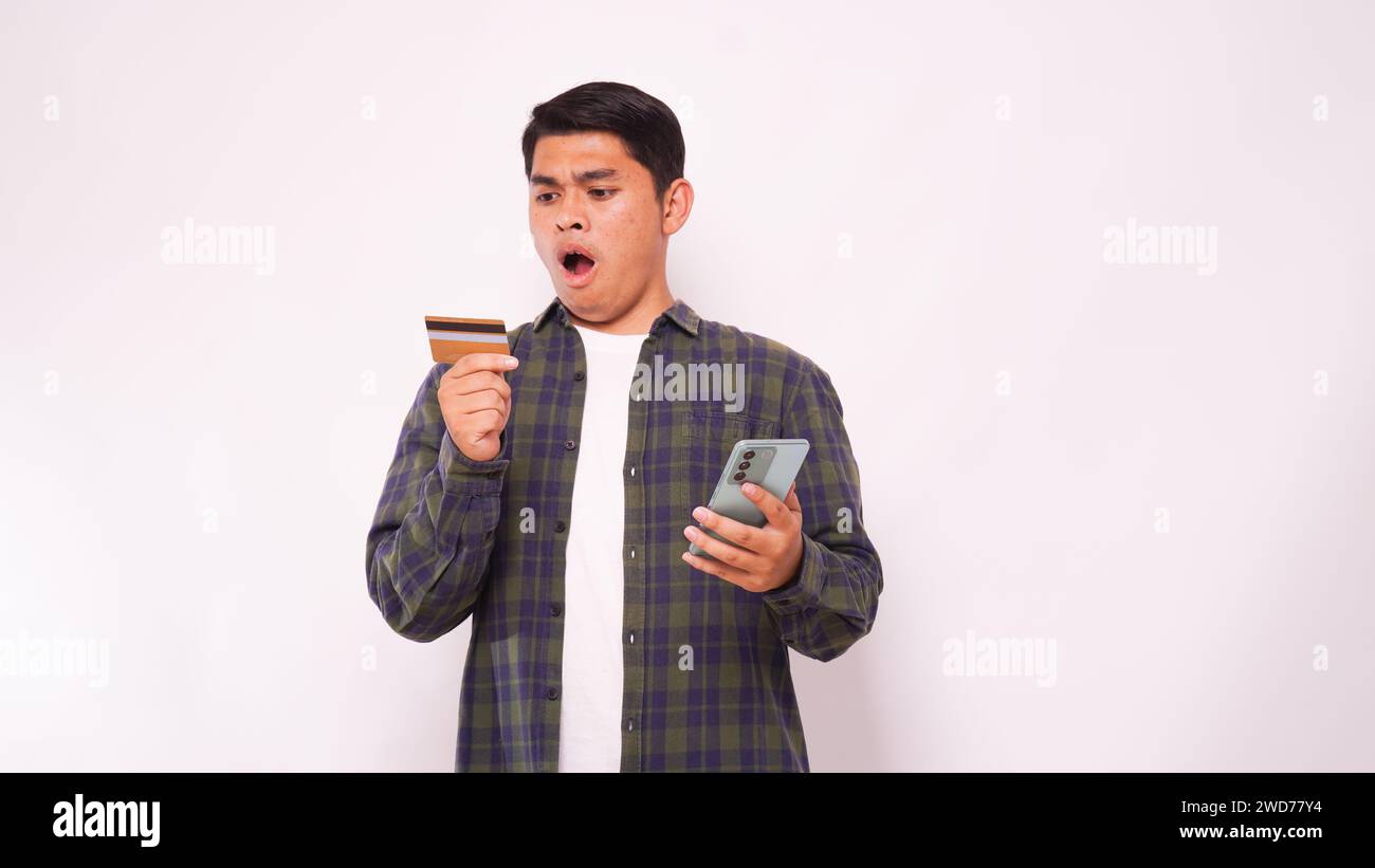 Asiatischer junger Mann mit Schockausdruck beim Bezahlen von Kreditkartenrechnungen Stockfoto
