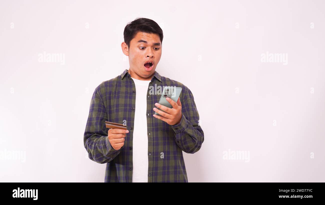 Asiatischer junger Mann mit Schockausdruck beim Bezahlen von Kreditkartenrechnungen Stockfoto