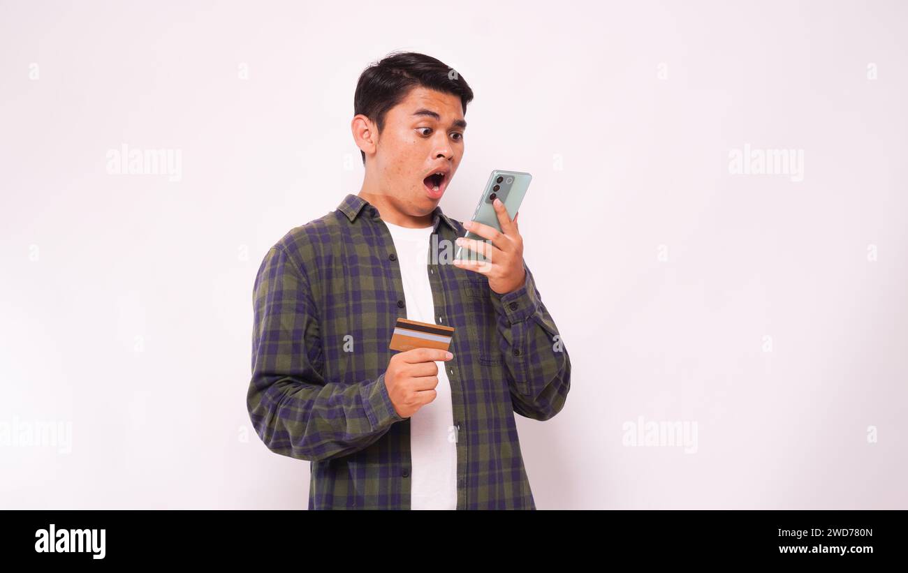 Asiatischer junger Mann mit Schockausdruck beim Bezahlen von Kreditkartenrechnungen Stockfoto