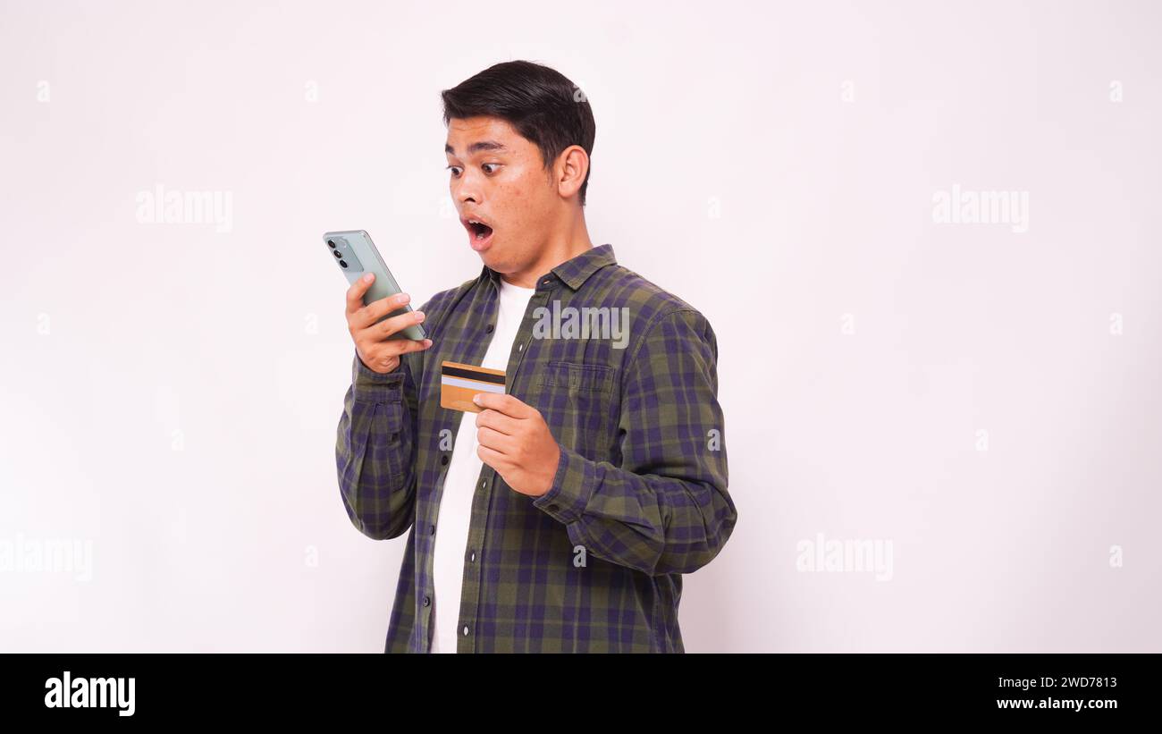 Asiatischer junger Mann mit Schockausdruck beim Bezahlen von Kreditkartenrechnungen Stockfoto