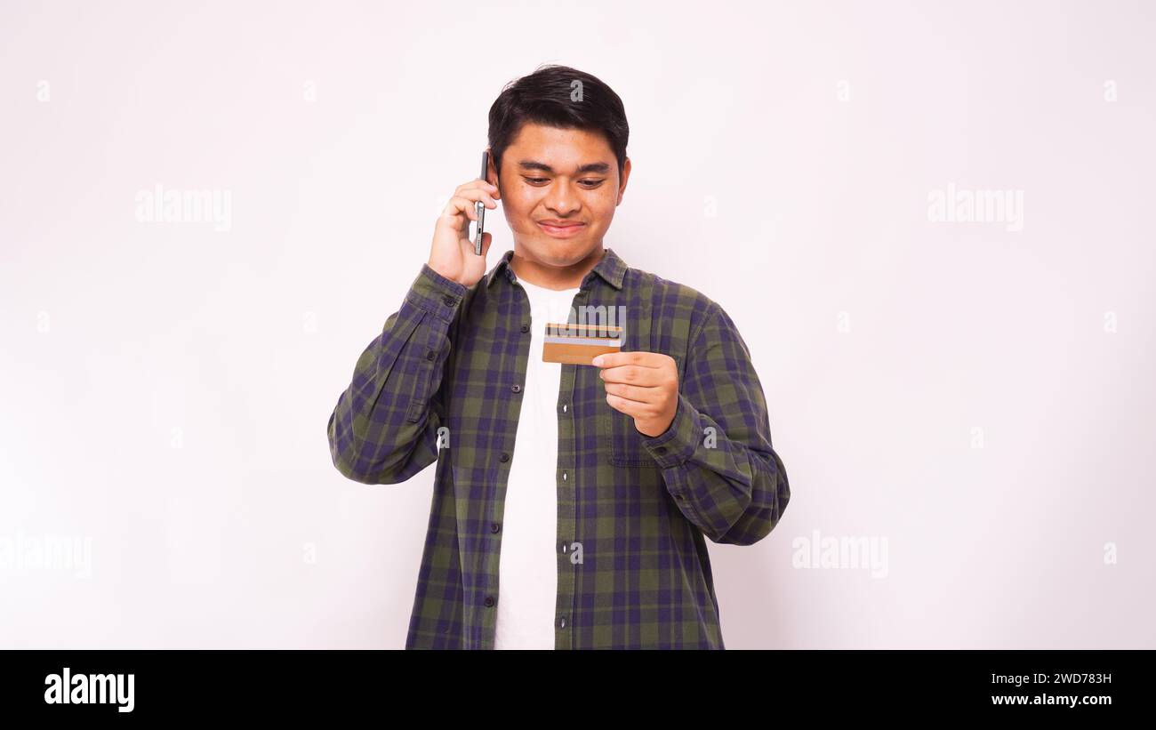 Asiatischer Mann lächelt beim Anruf und hält Kreditkarte über grauem Hintergrund Stockfoto