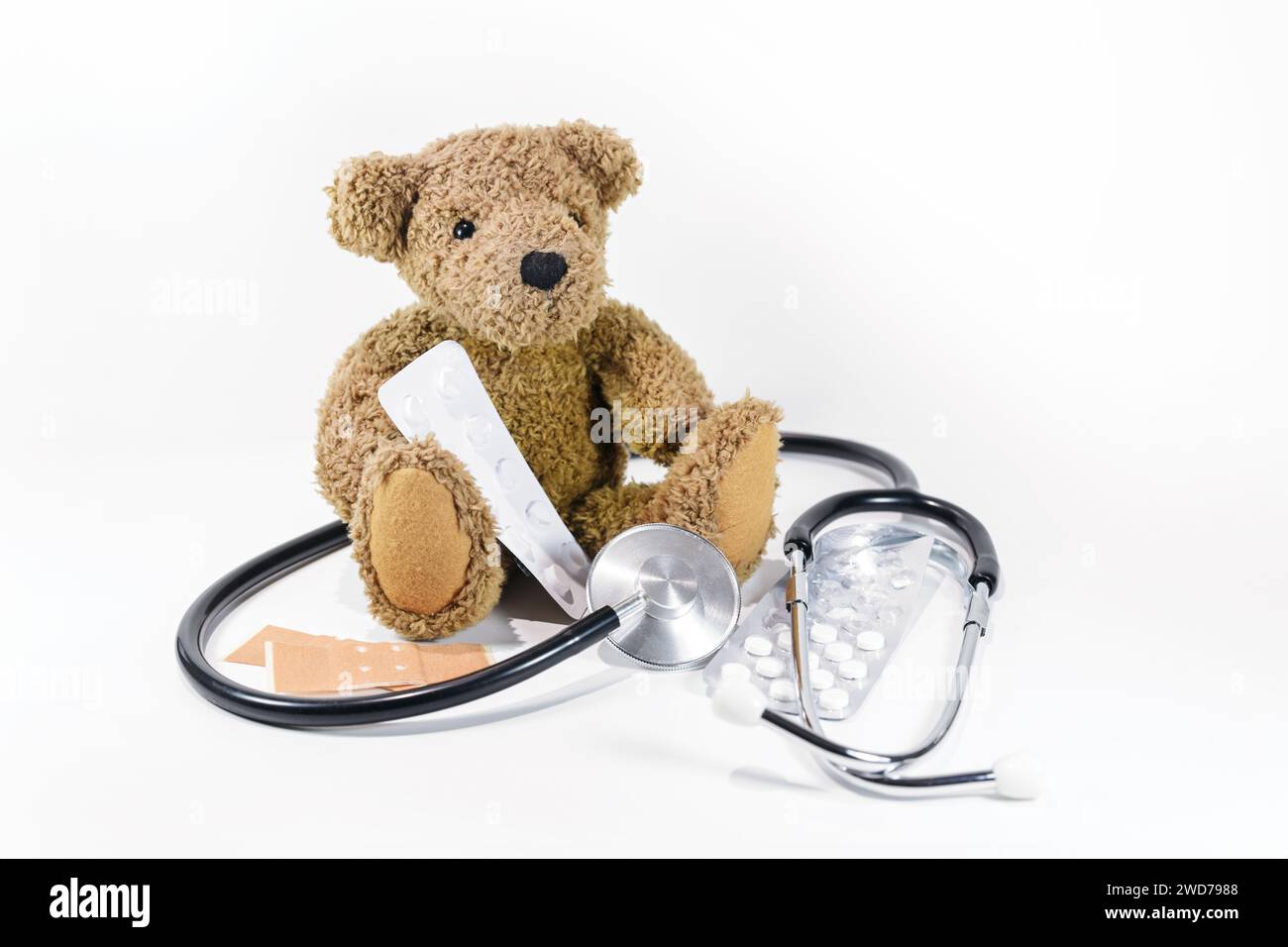 Teddybär sitzend mit Pillen, Gips und Stethoskop auf weißem Hintergrund, Gesundheitspflege für Kinder und Pädiatrie, aber auch Gefahr beim Spielen wi Stockfoto