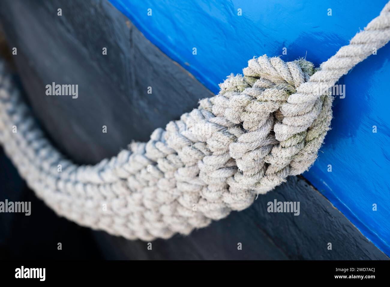 Ein dickes geflochtenes Seil hängt an der Seite eines blau lackierten Metallschiffes. Geringe Schärfentiefe Stockfoto