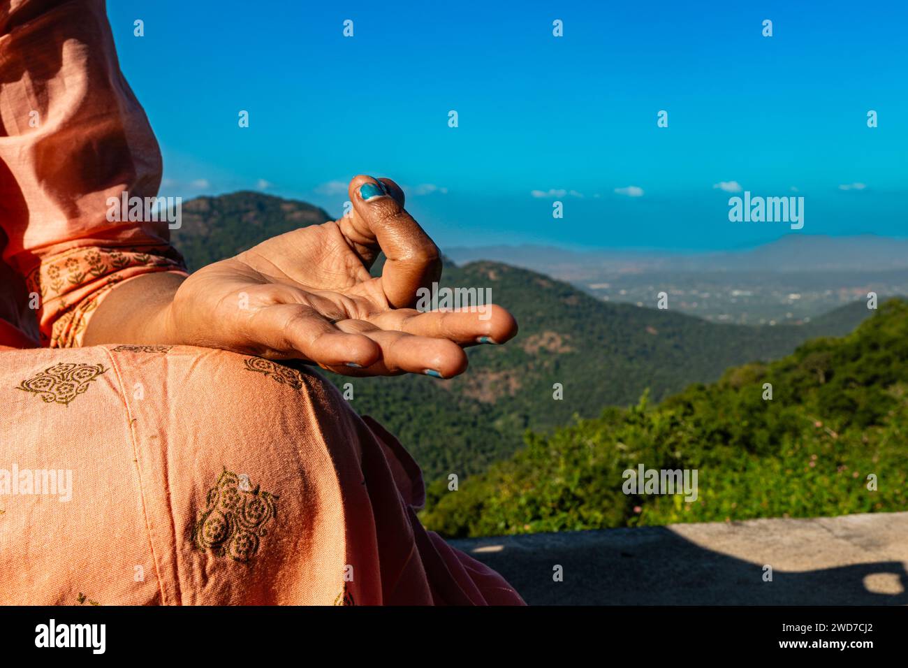 Eine Indianerin in traditioneller Kleidung findet Trost in Meditation auf einem majestätischen Berggipfel. Ihre Hände, anmutig in einer Mudra positioniert Stockfoto