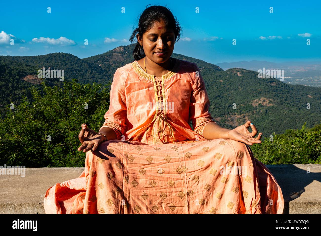 Eine Inderin in einem lebendigen Sari sucht Trost und spirituelle Verbindung durch Meditation inmitten der beeindruckenden Aussicht auf den Berg Stockfoto