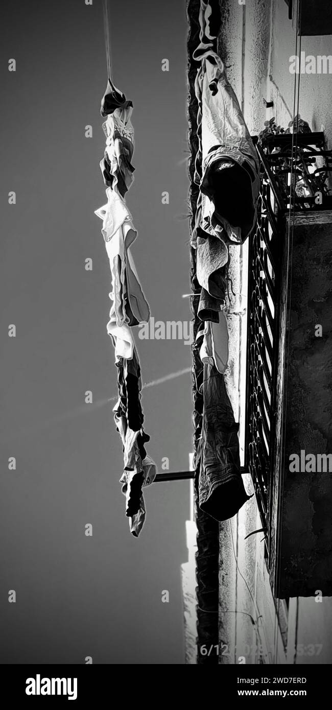 Dieses Schwarzweiß-Foto zeigt mehrere Kleidungsstücke, die an der Außenseite eines Gebäudes hängen Stockfoto