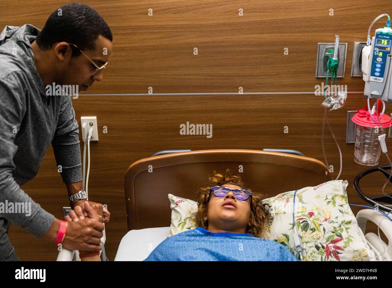 Multirassisches Paar hält die Hände während der Kontraktion bei der Geburt im Krankenhaus Stockfoto