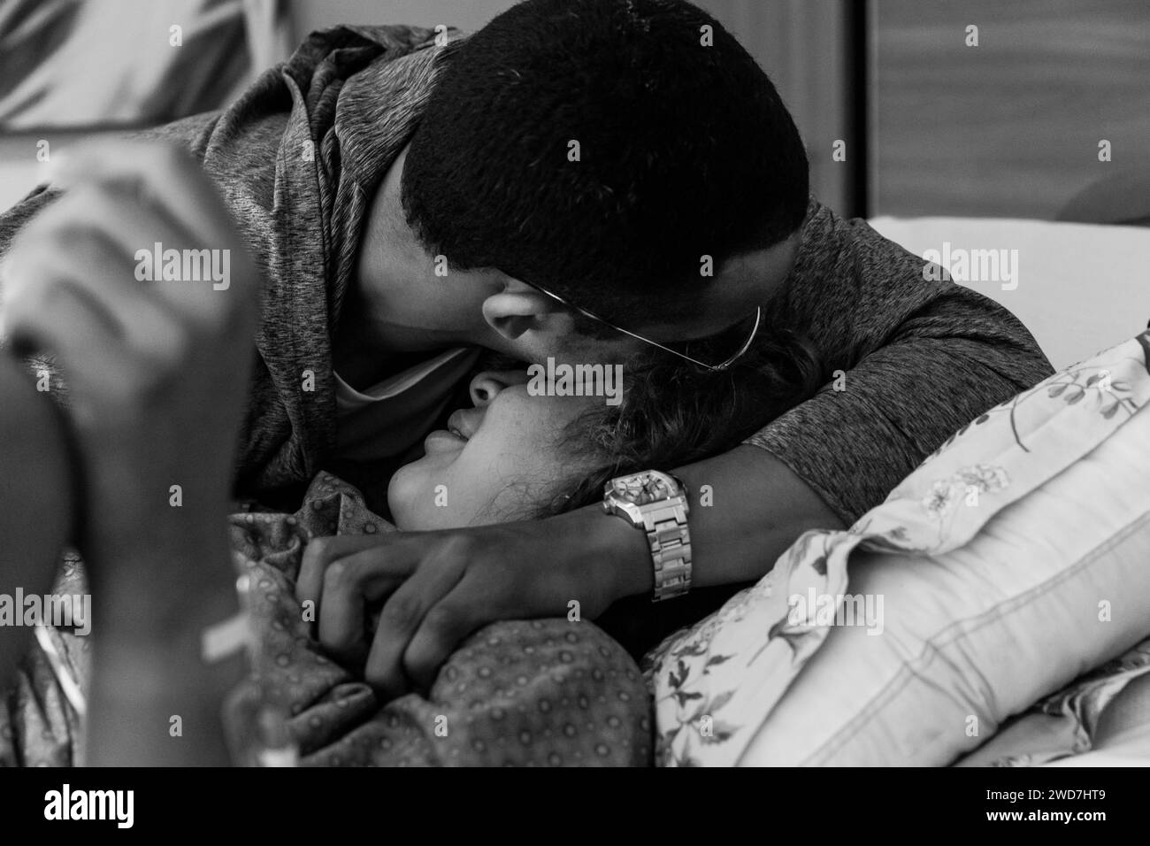 Multirassisches Ehepaar, das sich nach der Geburt im Krankenhauszimmer umschließt Stockfoto