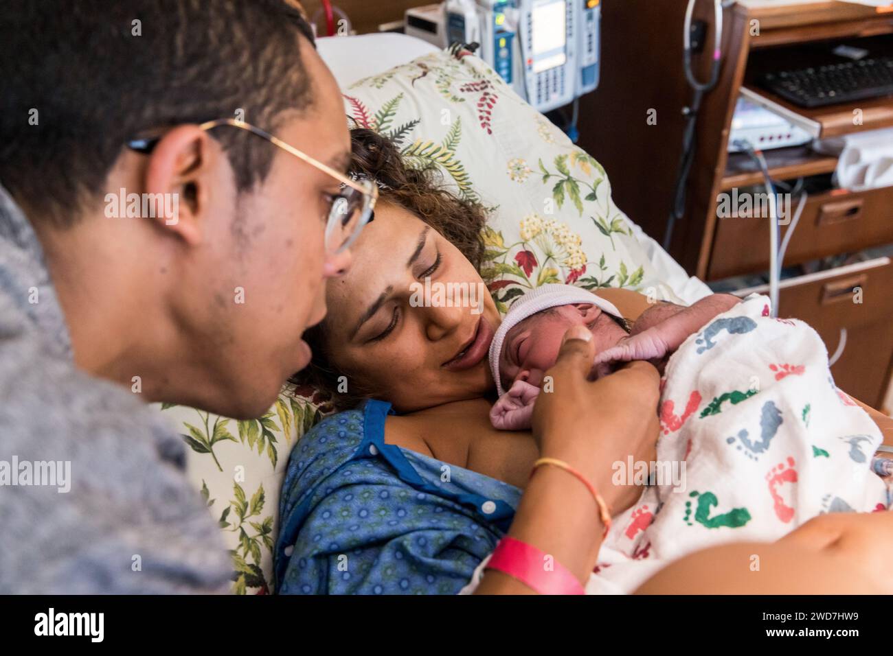 Multirassische Paare kuscheln sich direkt nach der Geburt im Krankenhaus an ihr Neugeborenes Stockfoto
