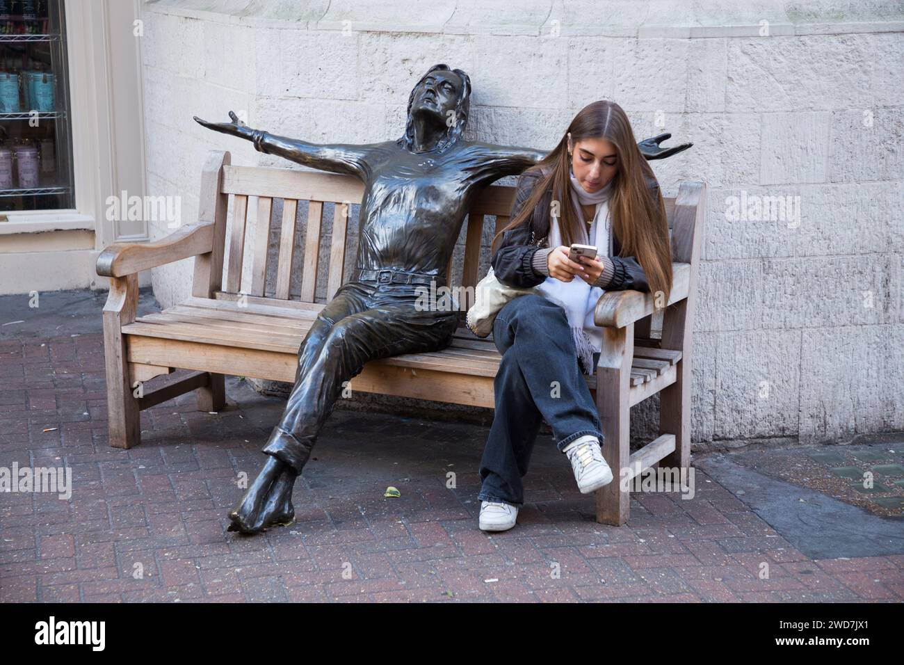 Weibliche Besucherin der Carnaby Street „in Conversation“ mit John Lennon Statue „Imagine“ von Bildhauer Lawrence Holofcener. London. UK. (137) Stockfoto