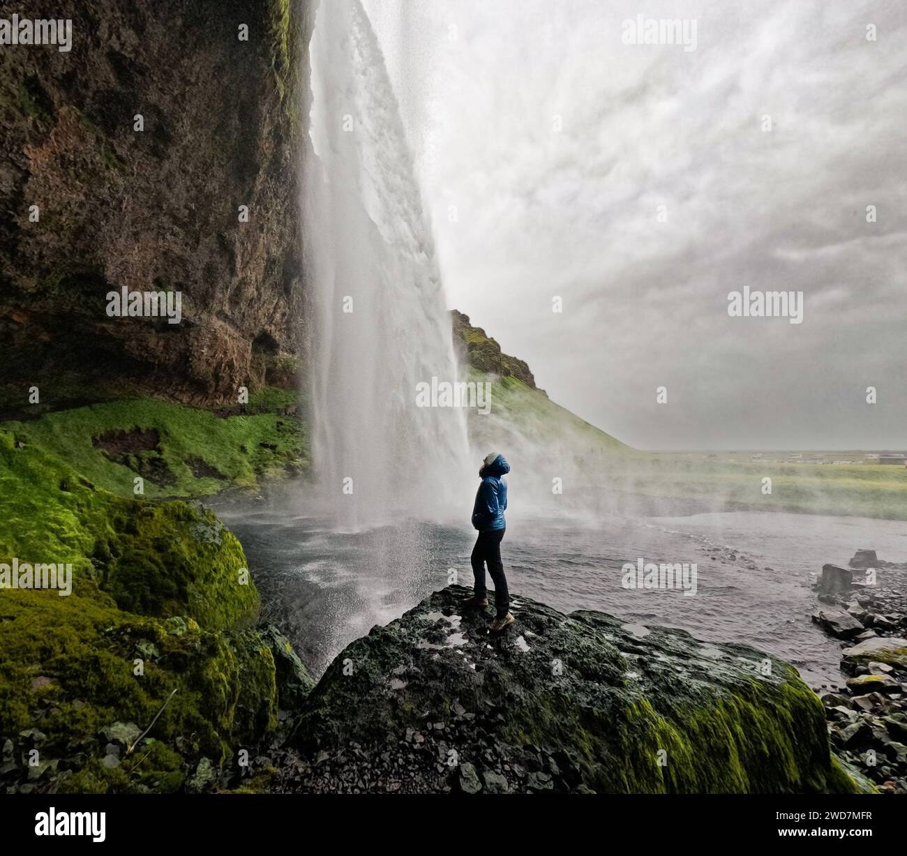 Frau wandert auf Felsen an einem riesigen Wasserfall mit grünen Hügeln herum Stockfoto