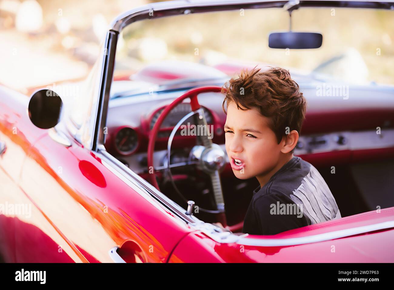 Junge, der im roten Oldtimer sitzt und so tut, als würde er fahren Stockfoto