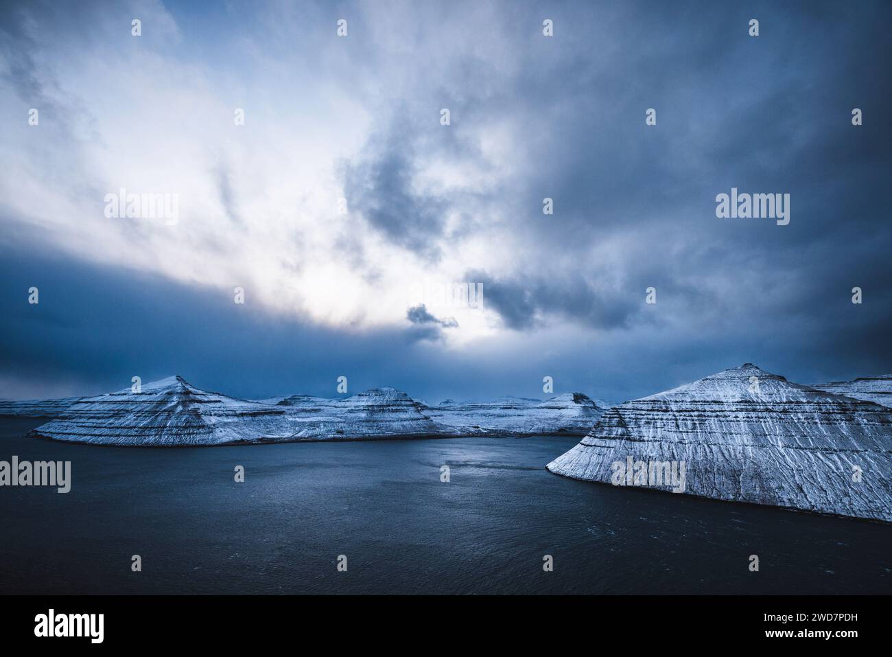 Dramatische Wolken über schneebedeckten Bergen und steilen Fjorden, Färöer Stockfoto