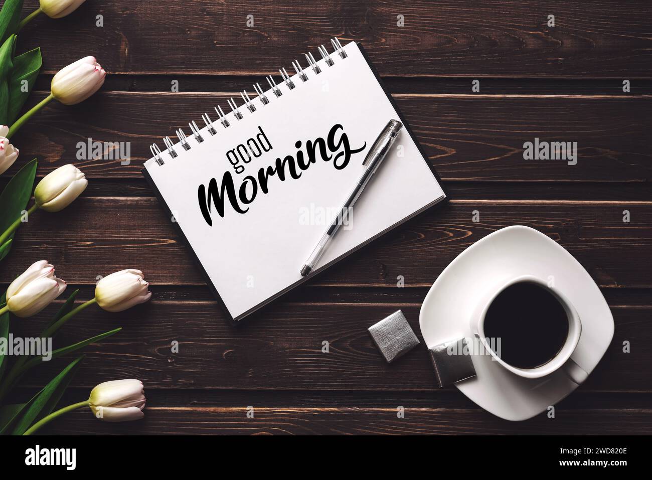 Grußkarte mit der Aufschrift Guten Morgen. Weiße Tulpen und eine Tasse Kaffee auf hölzernem Hintergrund Stockfoto