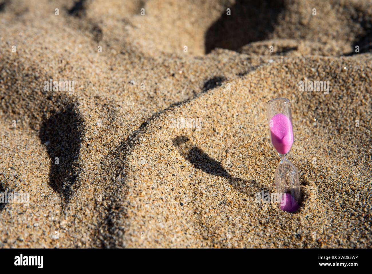 Rosafarbener Sand fällt anmutig in eine Sanduhr am Meer ab und fängt flüchtige Momente von ruhiger Schönheit am Strand ein Stockfoto