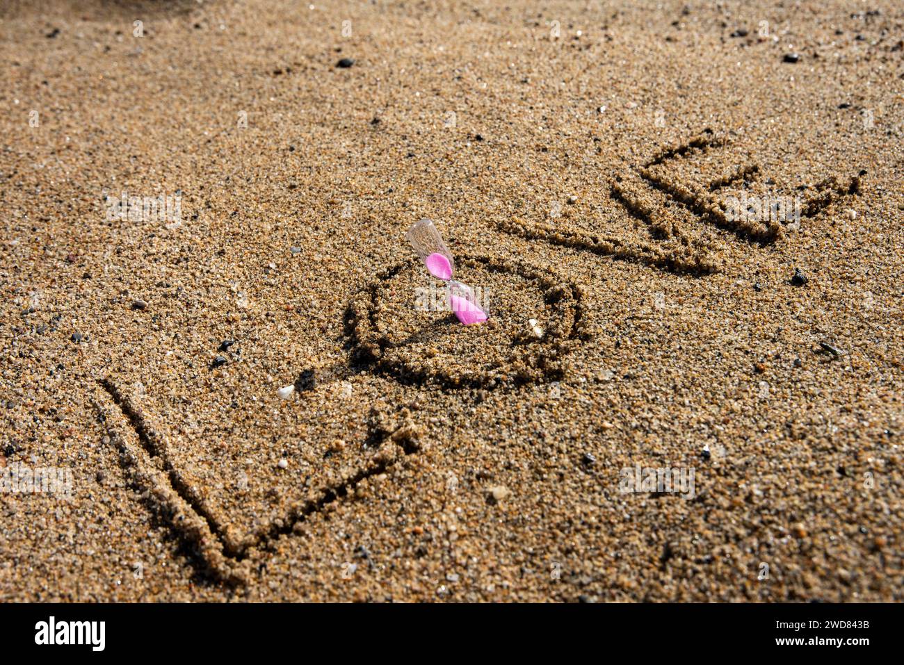 Zeitlose Liebe: „Liebe“ am Strand in einer rosafarbenen Sanduhr, wo Romantik auf den Sand ewiger Momente trifft Stockfoto