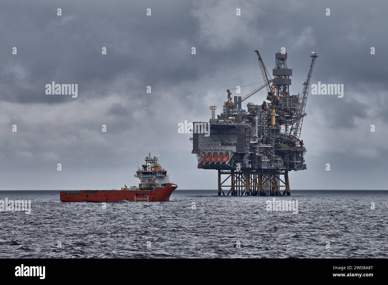Panoramablick auf die Jack Up Bohranlage und das Versorgungsschiff an einem dunklen bewölkten Tag im Meer. Erdöl- und Erdgasindustrie in der Nordsee. Stockfoto