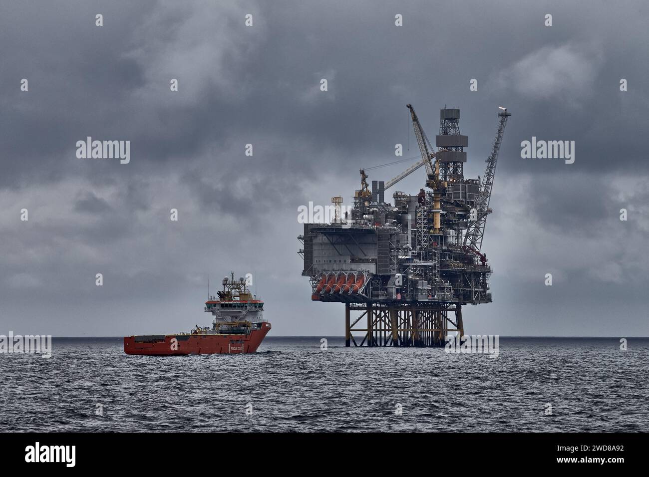 Panoramablick auf die Jack Up Bohranlage und das Versorgungsschiff an einem dunklen bewölkten Tag im Meer. Erdöl- und Erdgasindustrie in der Nordsee. Stockfoto