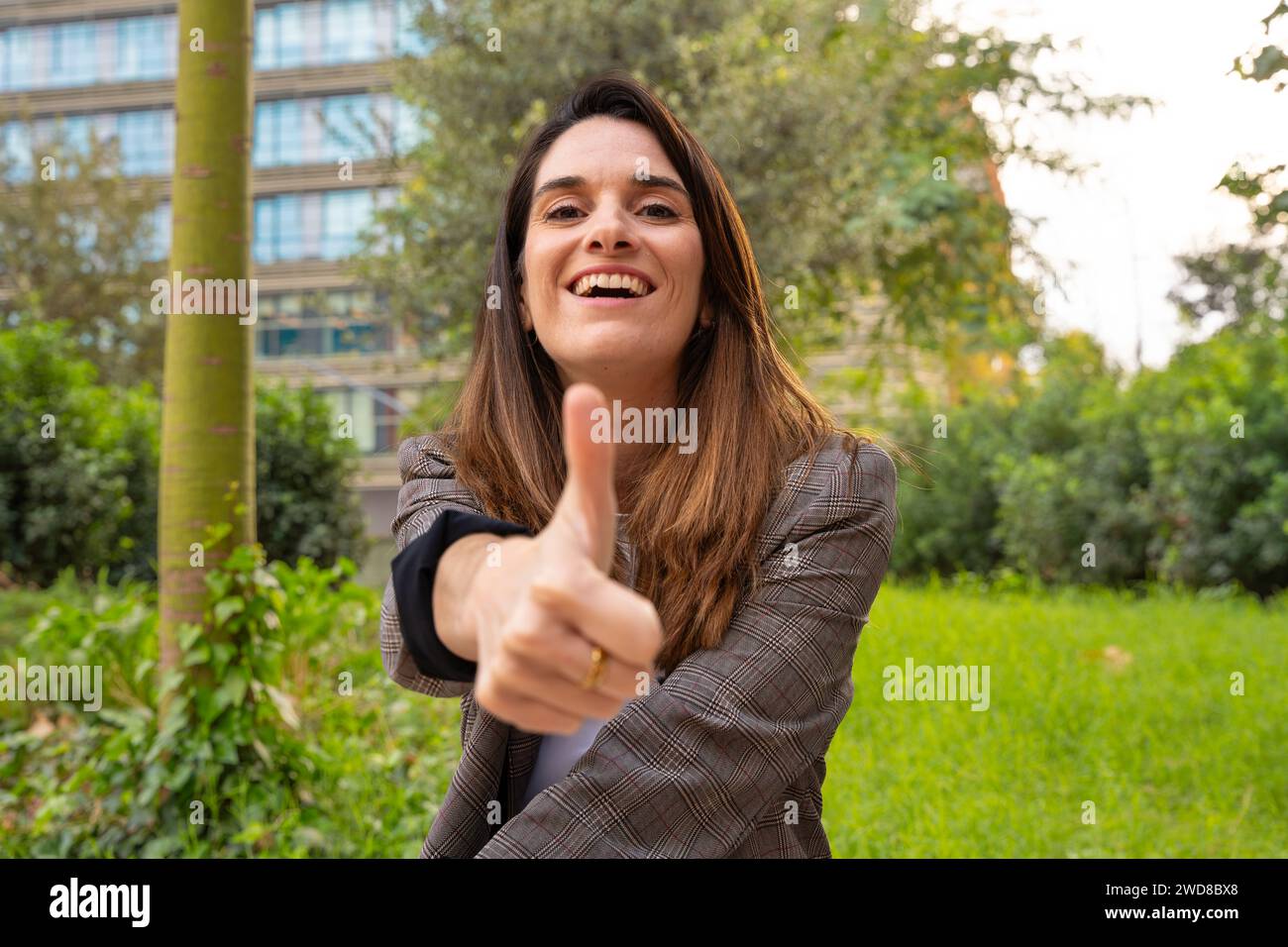 Porträt Junge Frau, die mit Daumen nach oben zeigt und draußen lächelnd in die Kamera blickt Stockfoto