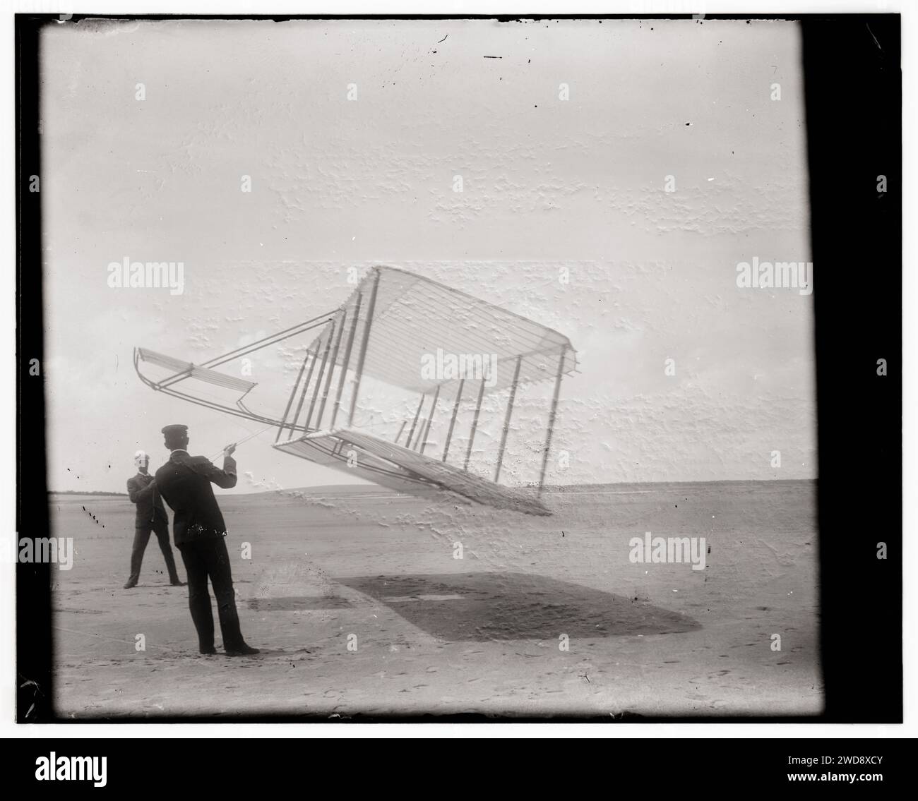 Geschichte der Luftfahrt - Wright Brothers - Seitenansicht des Segelflugzeugs, das als Drachen in Bodennähe fliegt, Wilbur links und Orville rechts, Segelflugzeug drehte sich vorwärts nach rechts und kippte nach unten, 1901 Stockfoto