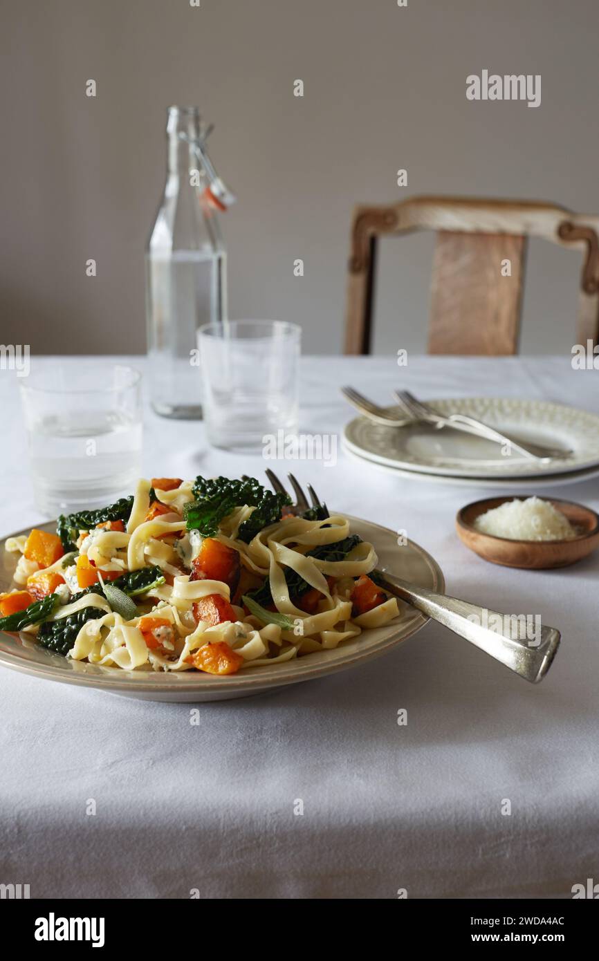 Tagliatelle mit gebratenem Butternusskürbis, Cavolo nero und Salbei, abgerundet mit Parmesan, serviert auf einem einfachen weißen Tisch. Stockfoto