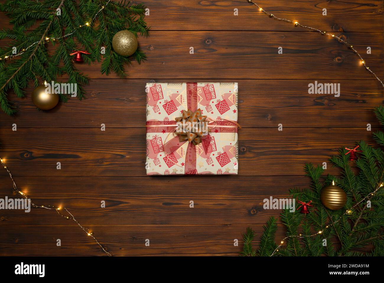 Weihnachtsgeschenkbox auf dunklem Holzhintergrund, eingerahmt von Tannenzweigen und Girlande. Stockfoto