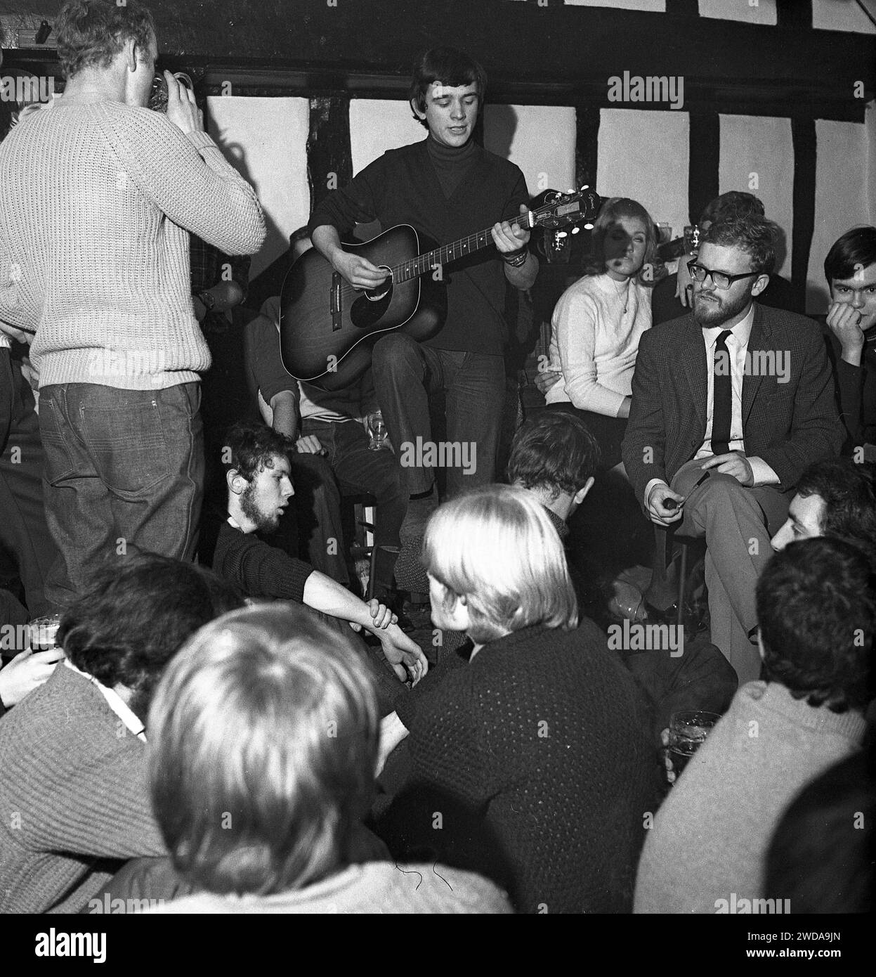 1960er Jahre, historische Folk-Jam-Session in einem Pub, ein junger Mann, der seine Gitarre spielt und im Publikum steht, England, Großbritannien. Stockfoto