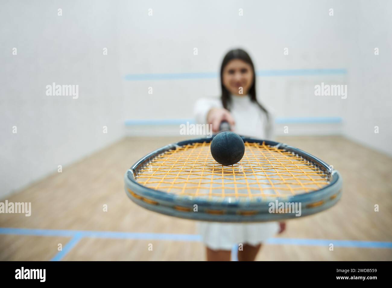 Lächelnde junge Frau spielt Squash und hält Schläger Stockfoto