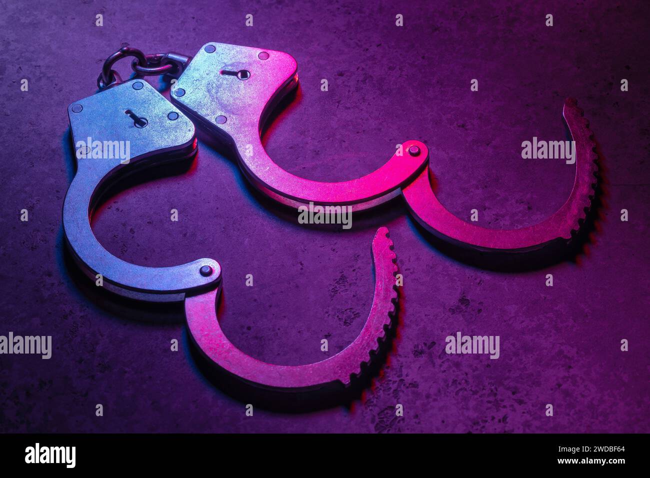 Offene Handschellen auf dunklem Hintergrund, beleuchtet mit einem farbigen gemischten Rot- und Blaulicht Stockfoto