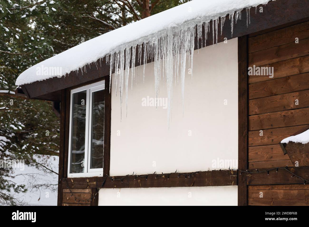 Schnee mit Eiszapfen auf dem Dach eines Gästehauses im Wald Stockfoto